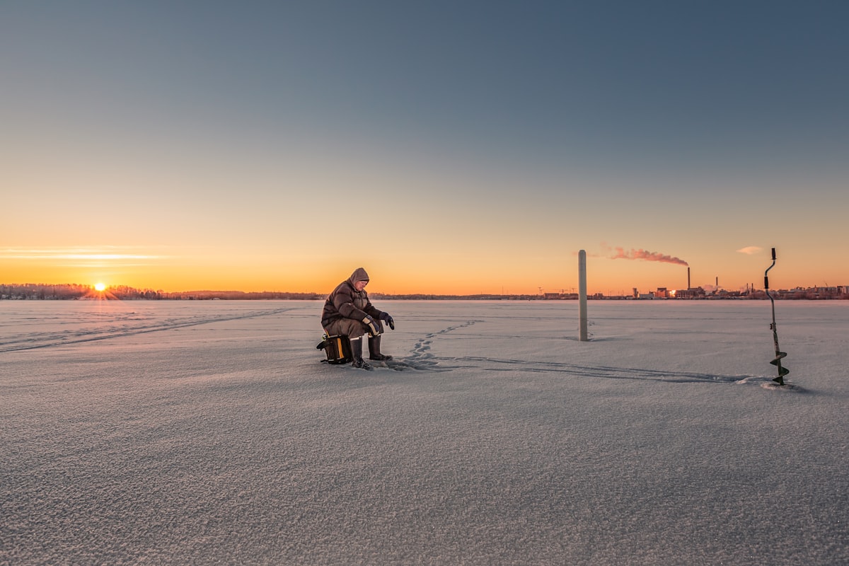 Person ice fishing with manual auger on frozen lake