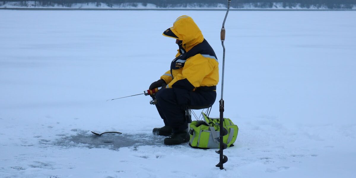 Man in yellow jacket ice fishing on frozen lake