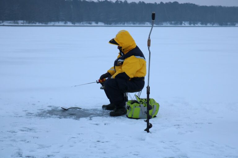 Man in yellow jacket ice fishing on frozen lake