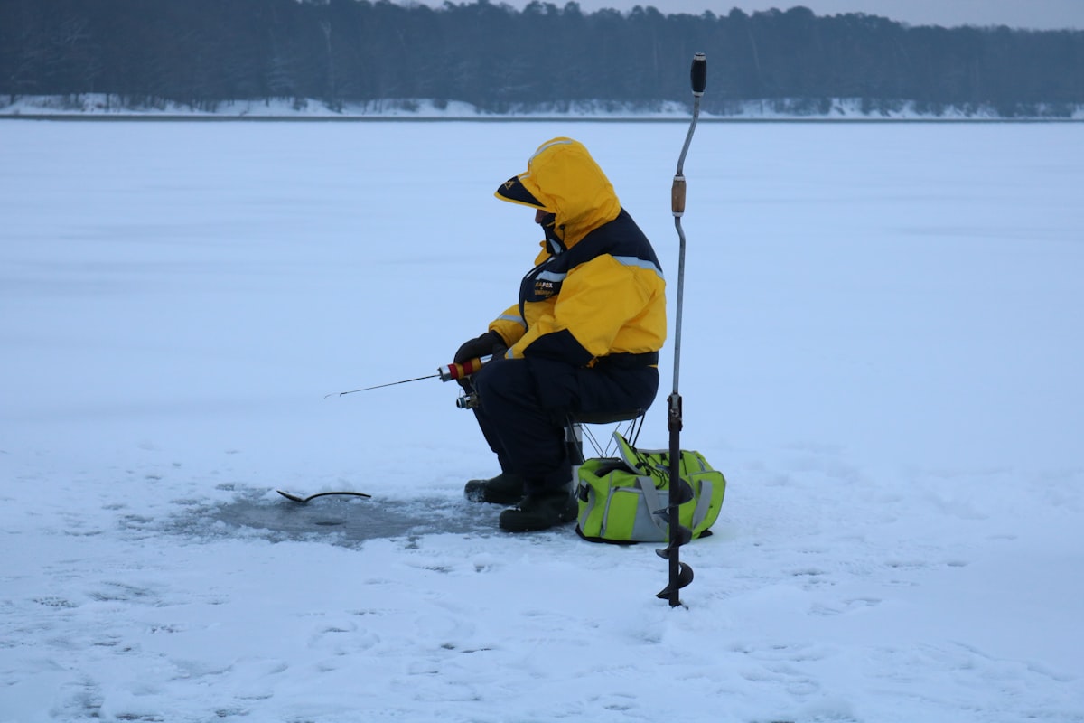Man in yellow jacket ice fishing on frozen lake